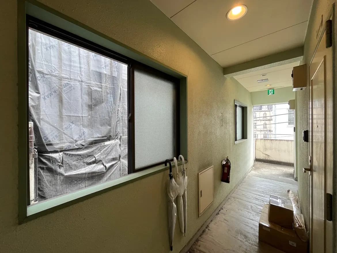 - グリーンの壁が印象的な廊下、窓から外の景色が見え、傘と消火器が配置された空間