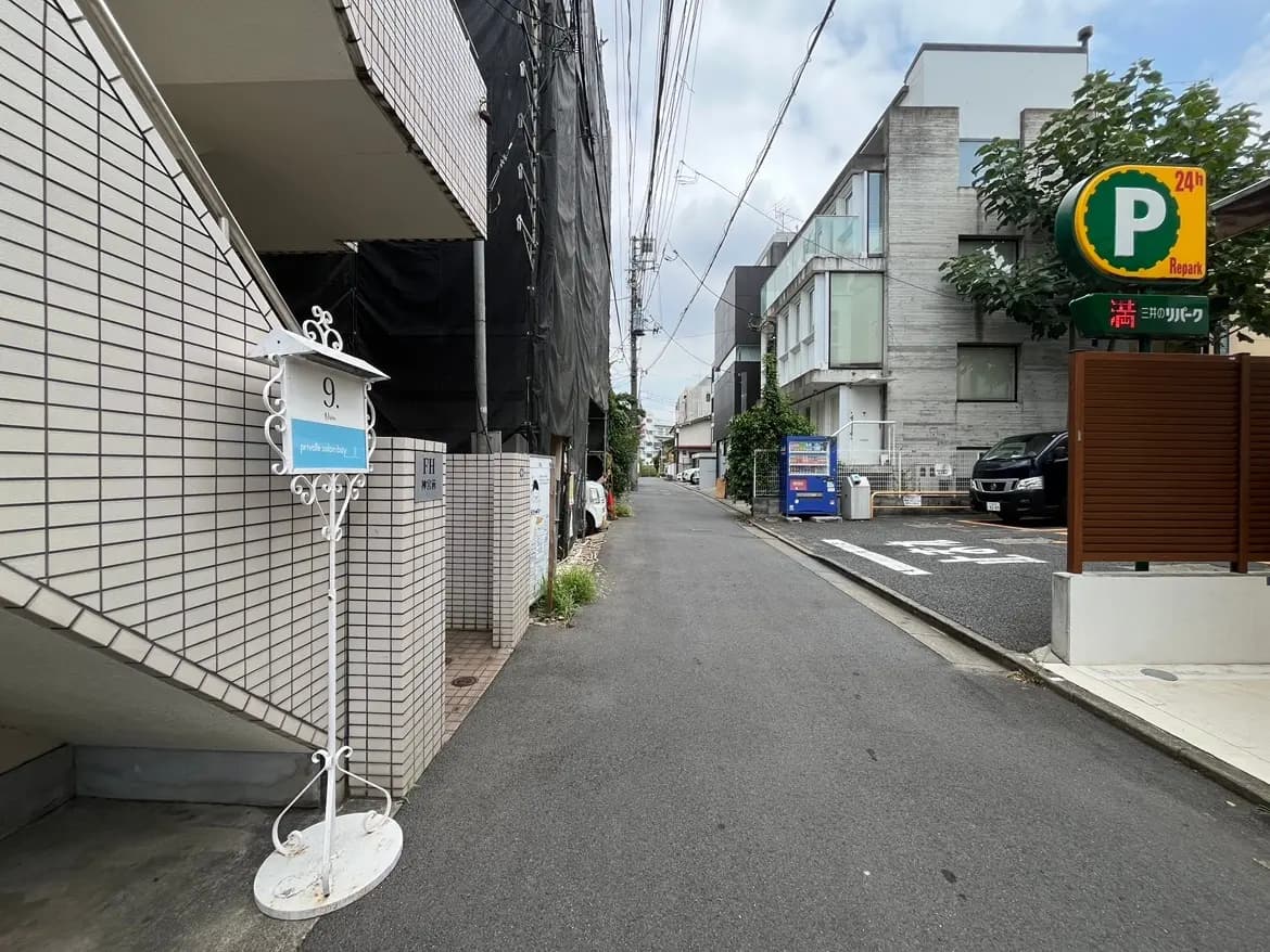 - 白いアイアン製の看板が立つアパートの階段、通りや建物が見える静かな街並み