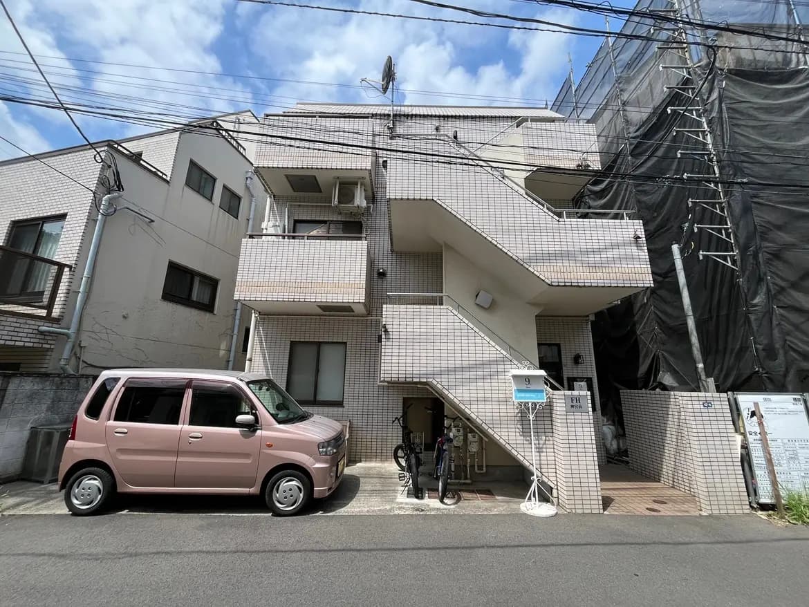 - 複数階建てのアパートメント、タイル張りの外観、ピンクの車と自転車が駐車されている通りの風景