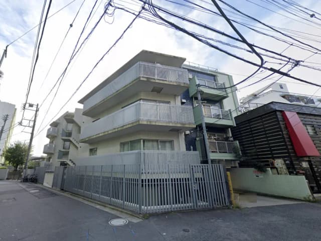 - 都市の住宅街にあるモダンなアパートメントビル、バルコニー付きの階層、周囲には電信柱やケーブルが見える風景