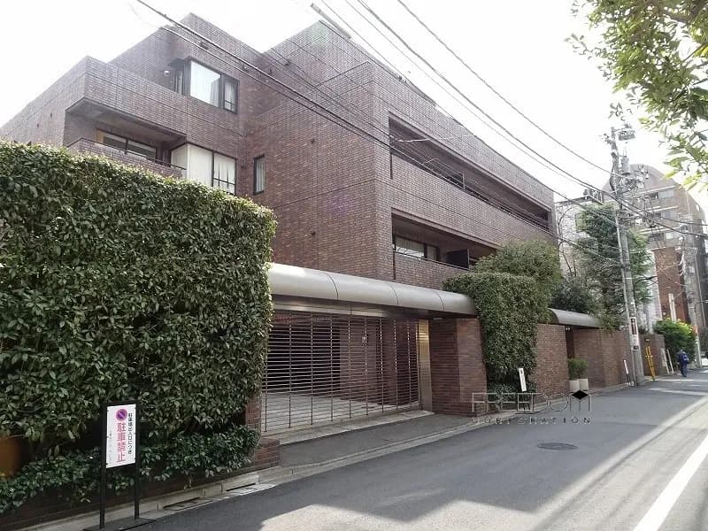 - 現代的なレンガ造りのマンション外観、周囲に緑の植栽と街路の様子、落ち着いた雰囲気のエリア