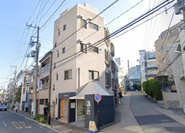 - 近代的な外観の建物、左側に駐車スペース、周囲に電線が走る閑静な街並み