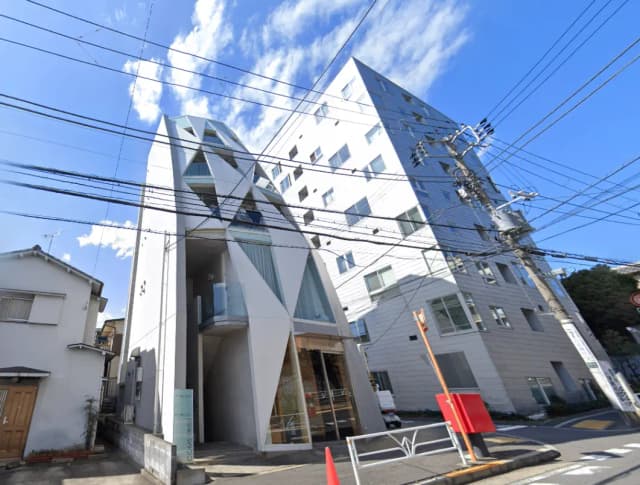 - 斬新なデザインの現代的なビル、白い外観と幾何学的な形状が特徴的で、青空を背景にした都市の風景