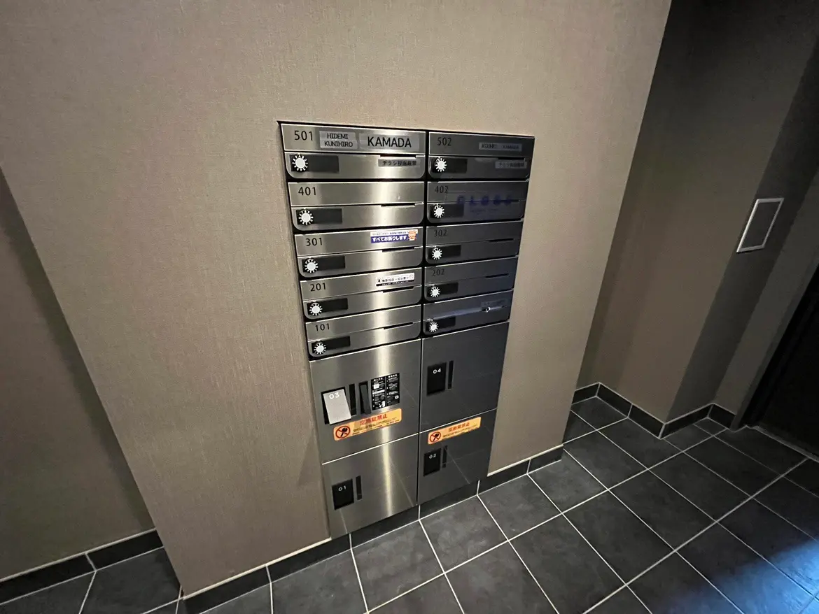 - 複数の郵便受けが並ぶマンションのロビー、各部屋番号と防犯対策のためのインターホンボタンが配置されたスタイリッシュなデザインの受け口