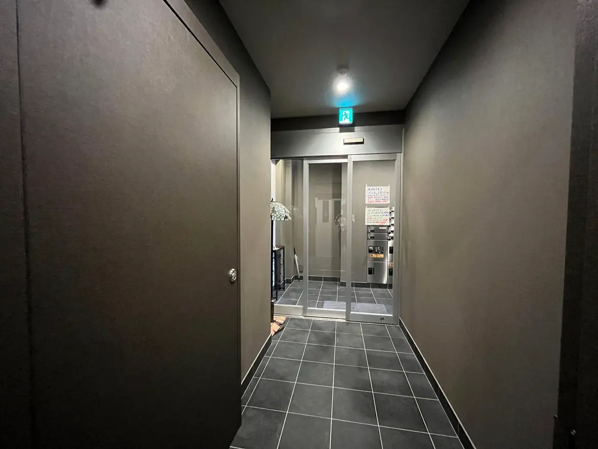 - モダンなデザインの暗い廊下、ダークな壁、タイル張りの床、クリアなガラス扉のエントランスが見える画像