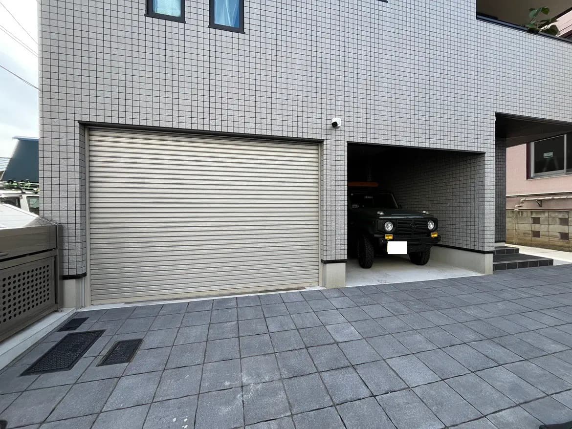 - 現代的な車庫の外観、シャッター付きのガレージとコンクリートの敷石、そこに駐車されている緑のSUV車の全景