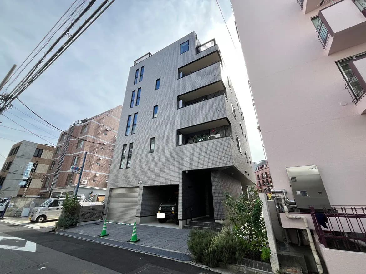 - シンプルな外観のアパートメントビル、隣接する建物と車が見える都会の風景、街路に面したエントランスが特徴的なデザイン