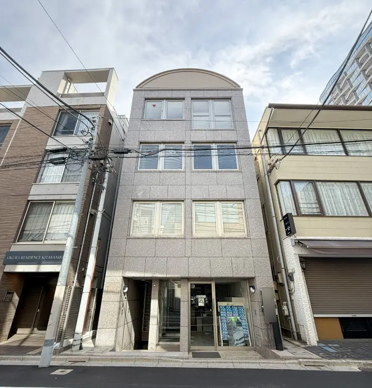 - 都市的な外観のオフィスビル、グレーの外壁、周囲の建物と電線が見える街並みの写真