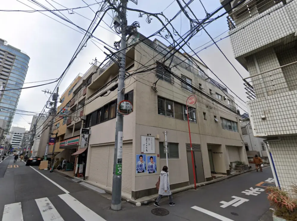 - 都市の路地に面した建物の外観、電柱と電線が交差し、店舗と住宅が共存する風景