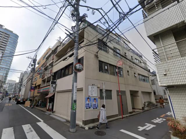 - 都市の路地に面した建物の外観、電柱と電線が交差し、店舗と住宅が共存する風景