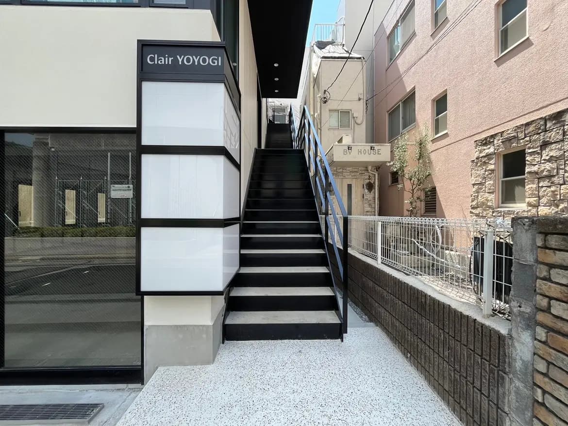 - Clair YOYOGIの建物外観、階段と黒い手すりが特徴的なエントランス、周囲に住宅が立ち並ぶ様子