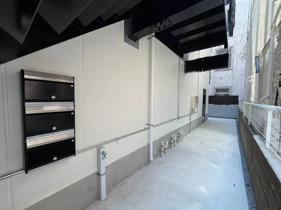 - モダンなデザインの建物の側面、黒の郵便ポストが並び、屋外の通路と白い壁が映える風景