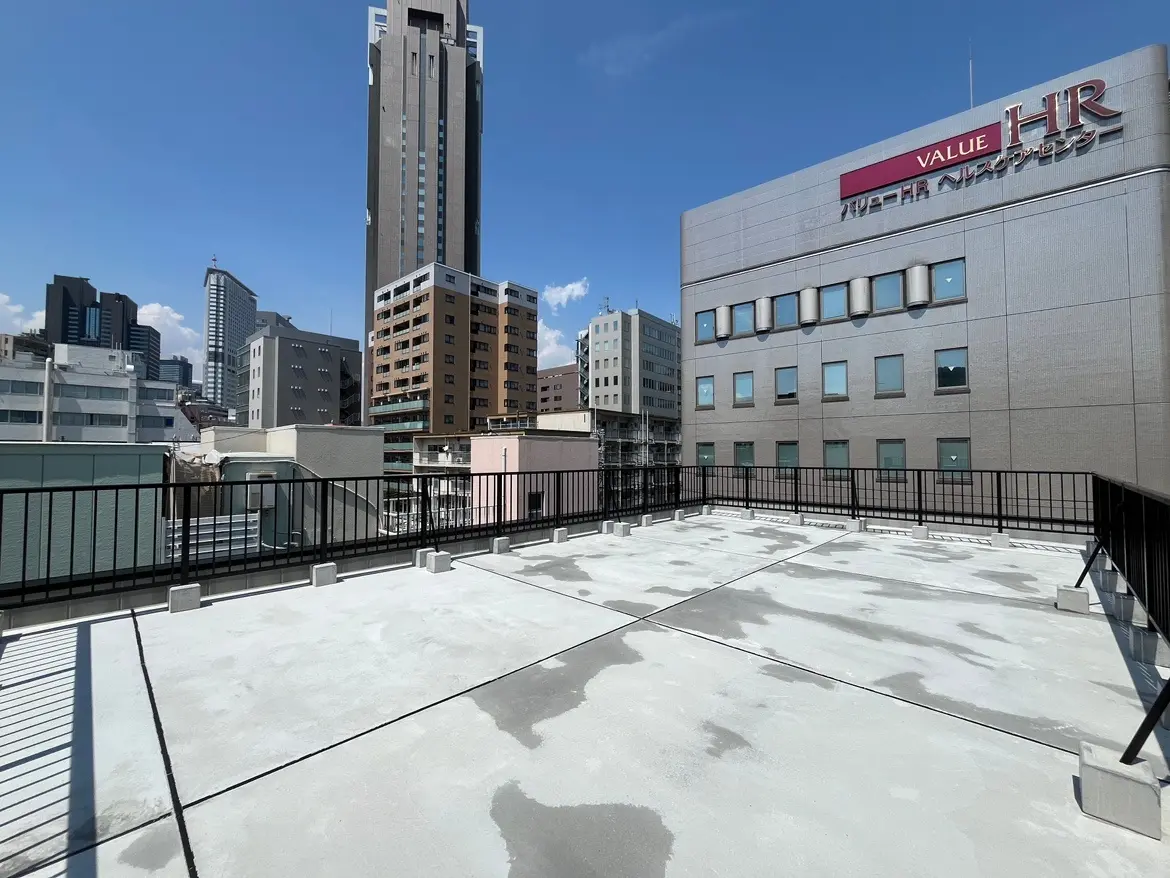 - ビルの屋上からの都市景観、近くの建物と青空、広いスペースが見える屋上 terrace