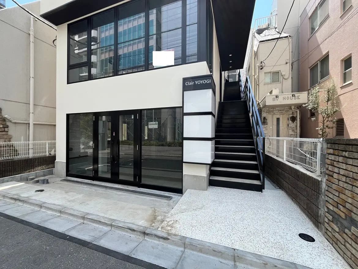 - モダンな外観の建物、黒いフレームの大きな窓、白い壁と特徴的な階段があるエントランスの風景