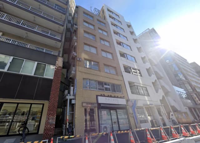 - 都市的な風景の中に立つ複数のビル、正面には「Kalani」の看板が設置された店舗、道路工事のためのバリケードが並んでいる様子
