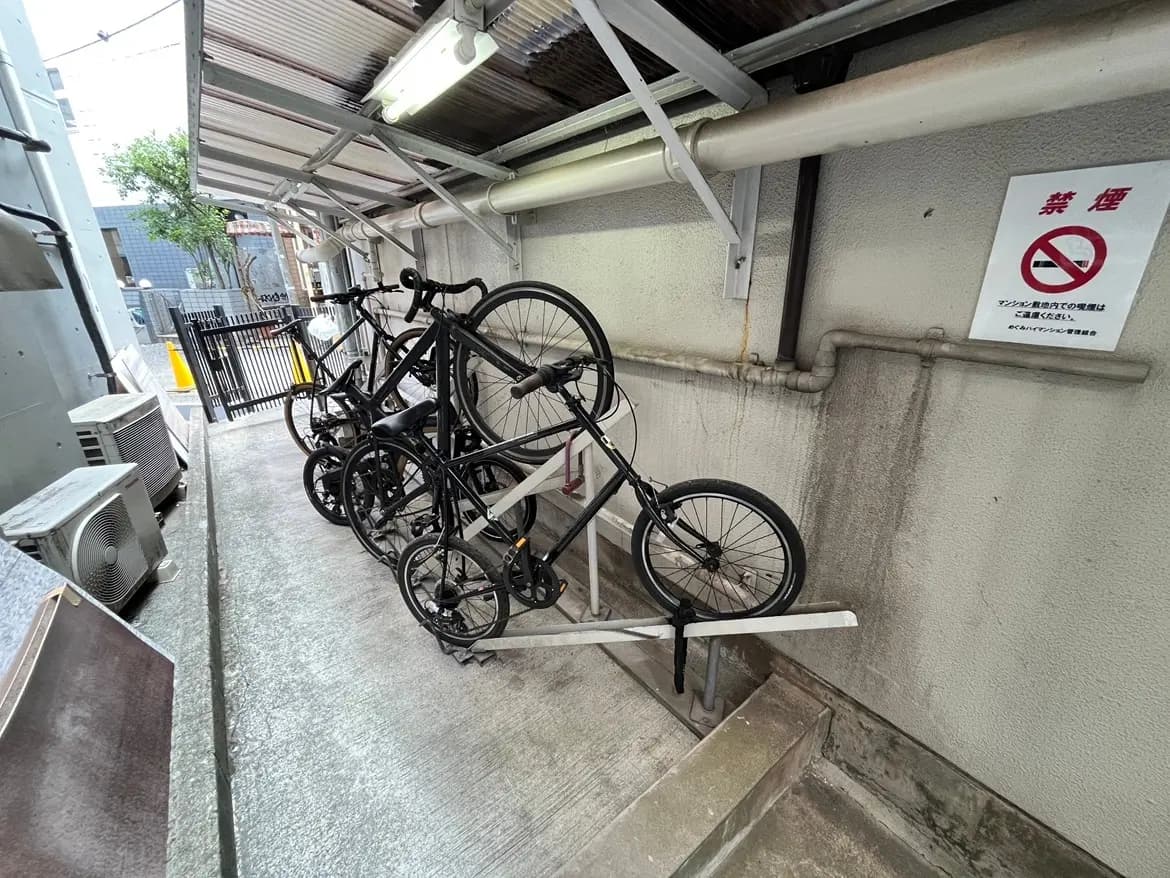 - 壁に寄せられた自転車が収納された屋外スペース、禁煙の注意書きが掲示されている様子