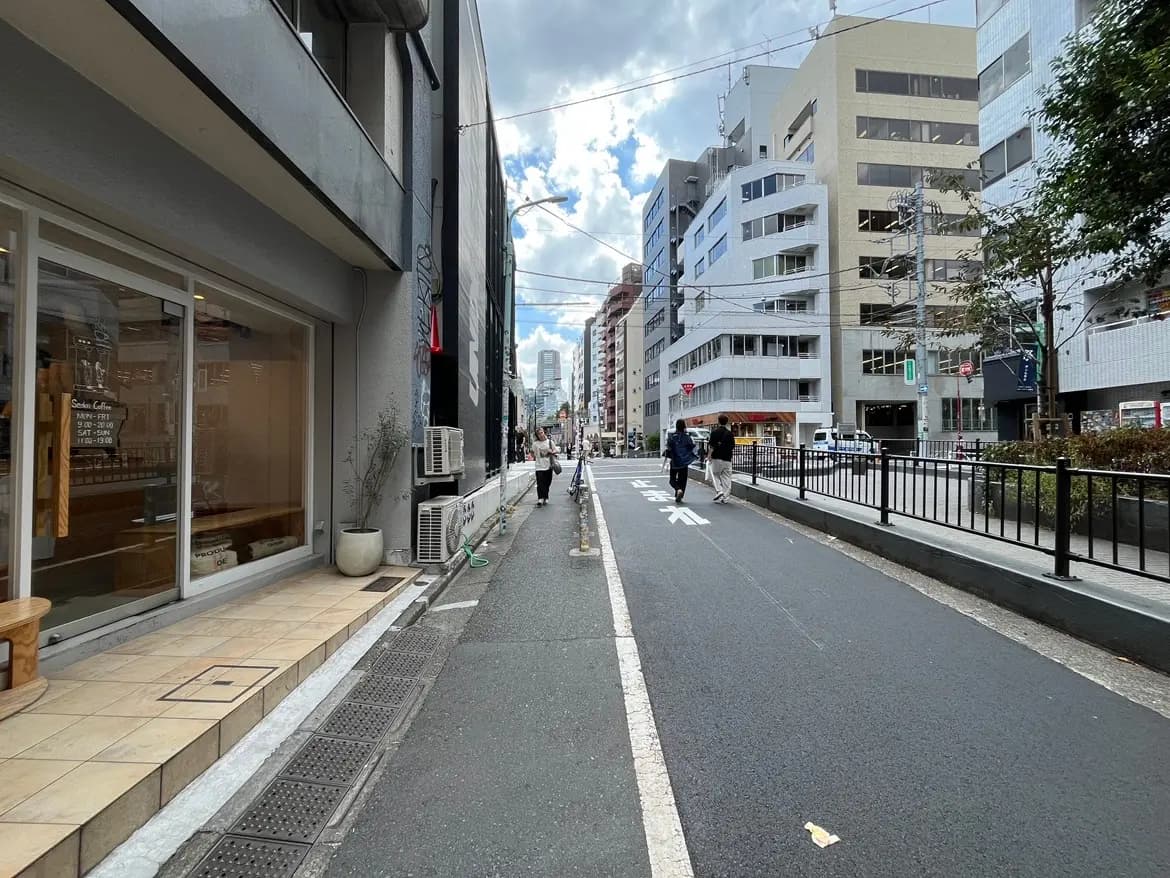 - 都会の通り、カフェの外観と並ぶビル群、歩行者が行き交う風景、曇り空の下の街並み