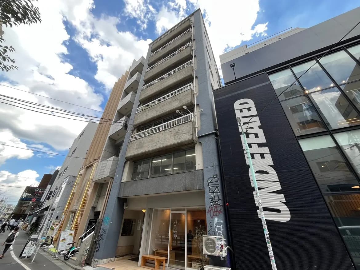 - モダンなデザインの建物が立ち並ぶ通り、青空と白い雲を背景にした「UNDEFEATED」というブランド名の看板が目立つ画像