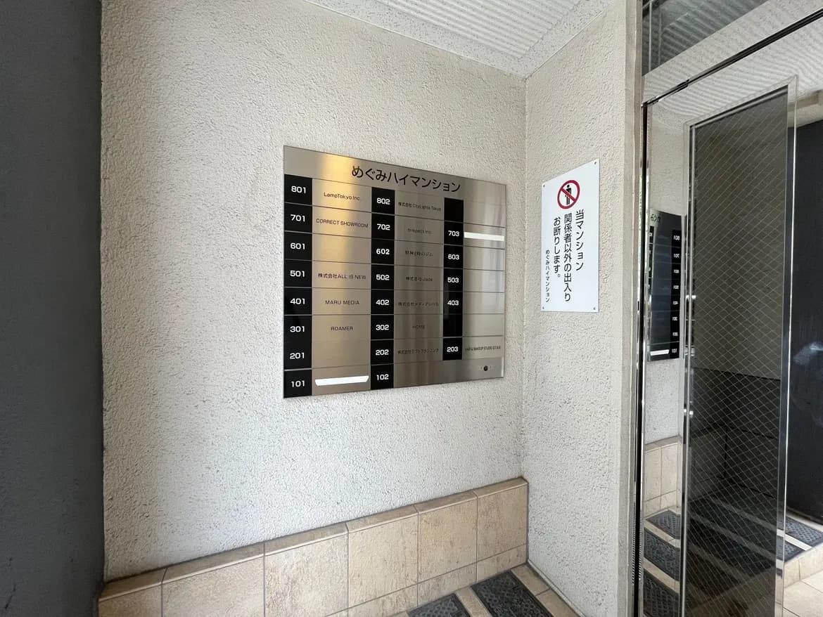- 入口付近にあるマンションの部屋番号案内板、周囲の壁と床のデザインが写る内部の様子