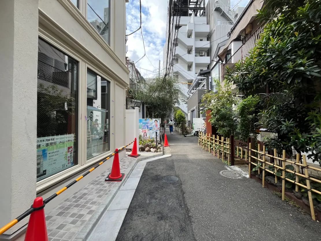 - 街中の狭い通り、両側に立ち並ぶ建物と竹のフェンス、赤いコーンが並ぶ風景