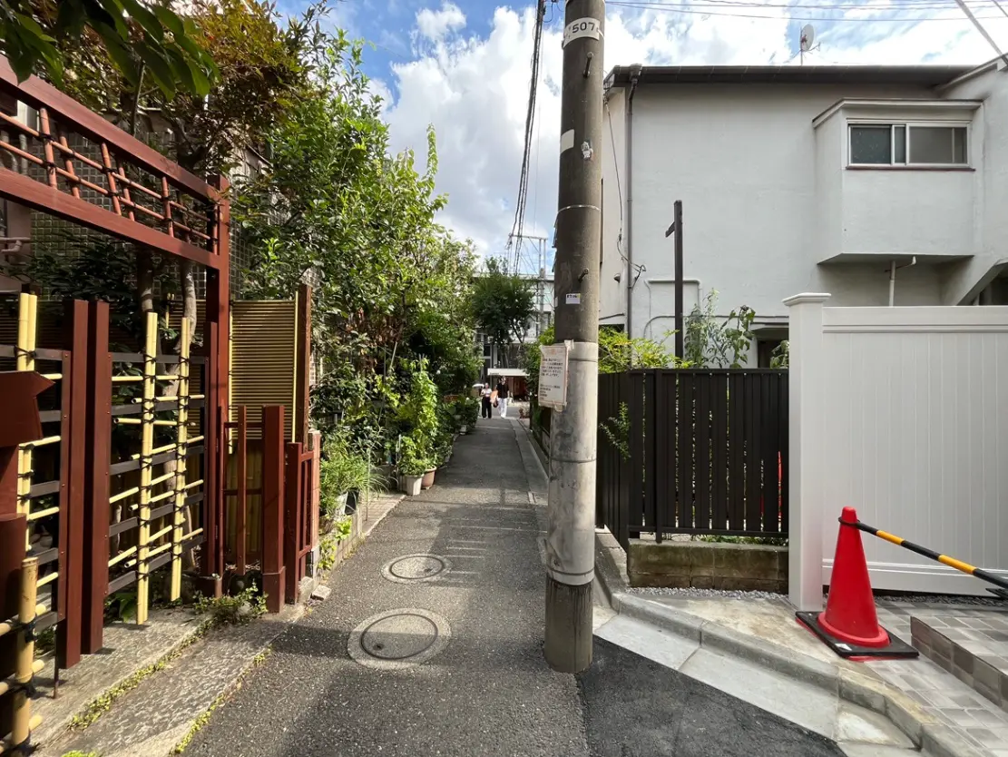 - 緑に囲まれた静かな路地、竹のフェンスと白い囲い、道路には交通標識とコーンが設置された風景
