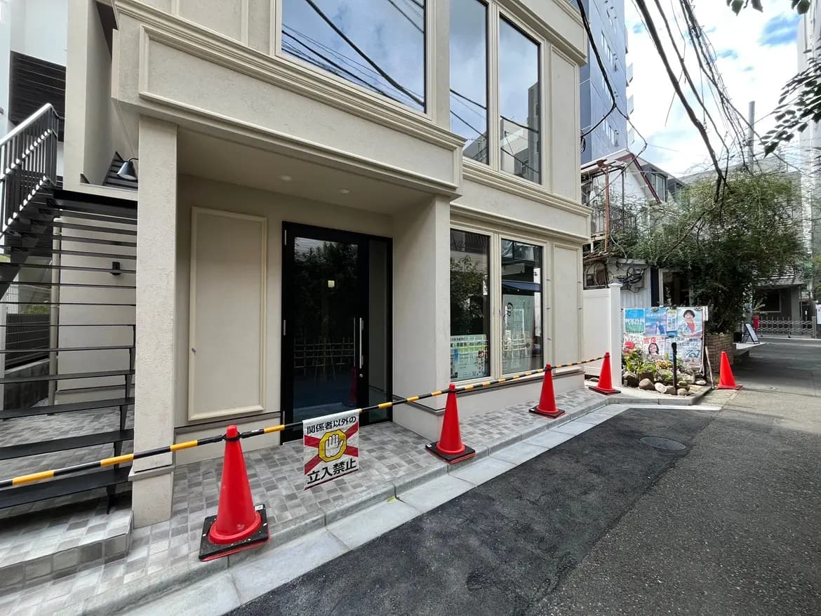 - 外分譲マンションのエントランス、周囲に赤いコーンが並び、立入禁止の看板が掲示されている様子