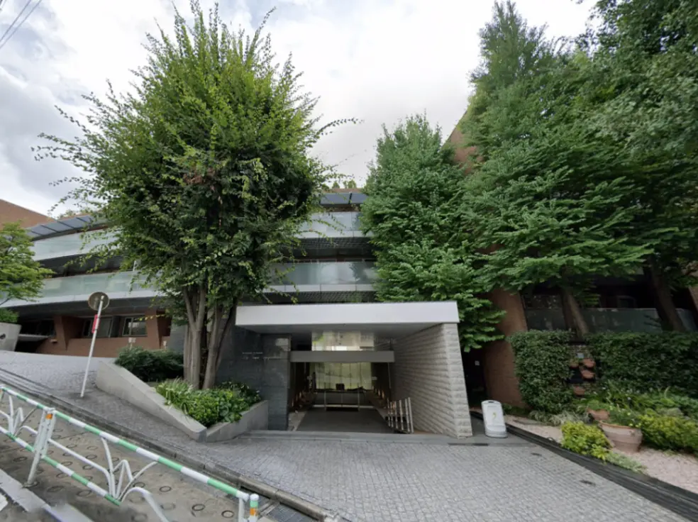 - 自然に囲まれたモダンな建物のエントランス、緑豊かな植栽とスロープのある外観