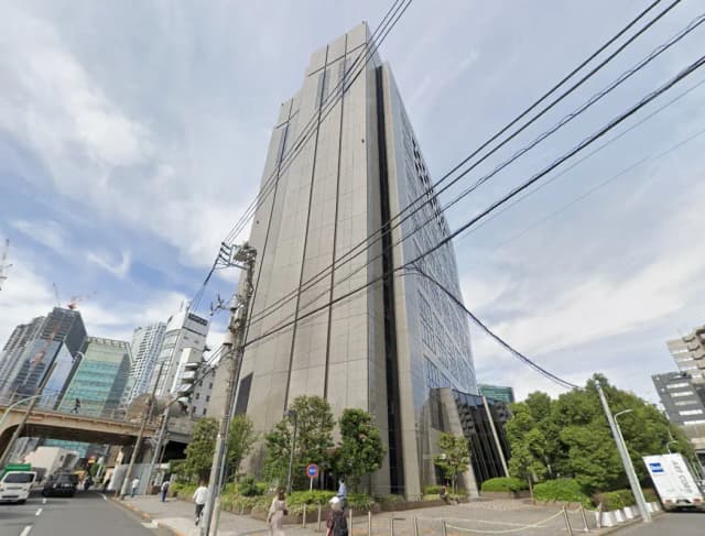 - 高層ビルの外観、周囲の街並みと道路、電柱や電線が見える都市景観