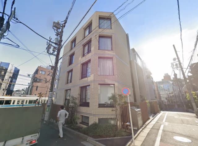 - 明るい日差しの中、外観が特徴的なモダンな建物、周囲には電線や街の風景が広がるシーン