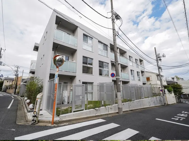 - モダンなデザインのアパート外観、バルコニー付きの窓、周辺には植栽と道路がある景観
