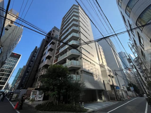 - 都市部に建つ現代的な高層マンション、周囲に高層ビルが立ち並び、青空が広がる風景
