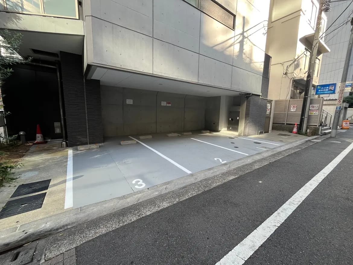 - モダンなコンクリートビルの駐車場、空きスペースが番号で表示され、道路に面した静かな環境
