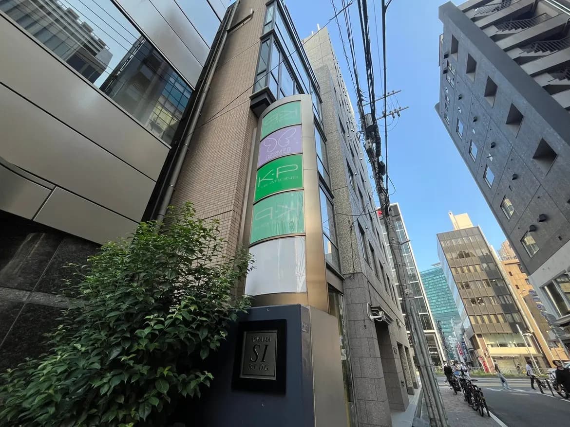 - 近代的なビルの外観、ストリートサインと青空を背景にした都市風景、緑の植物が添えられた一画