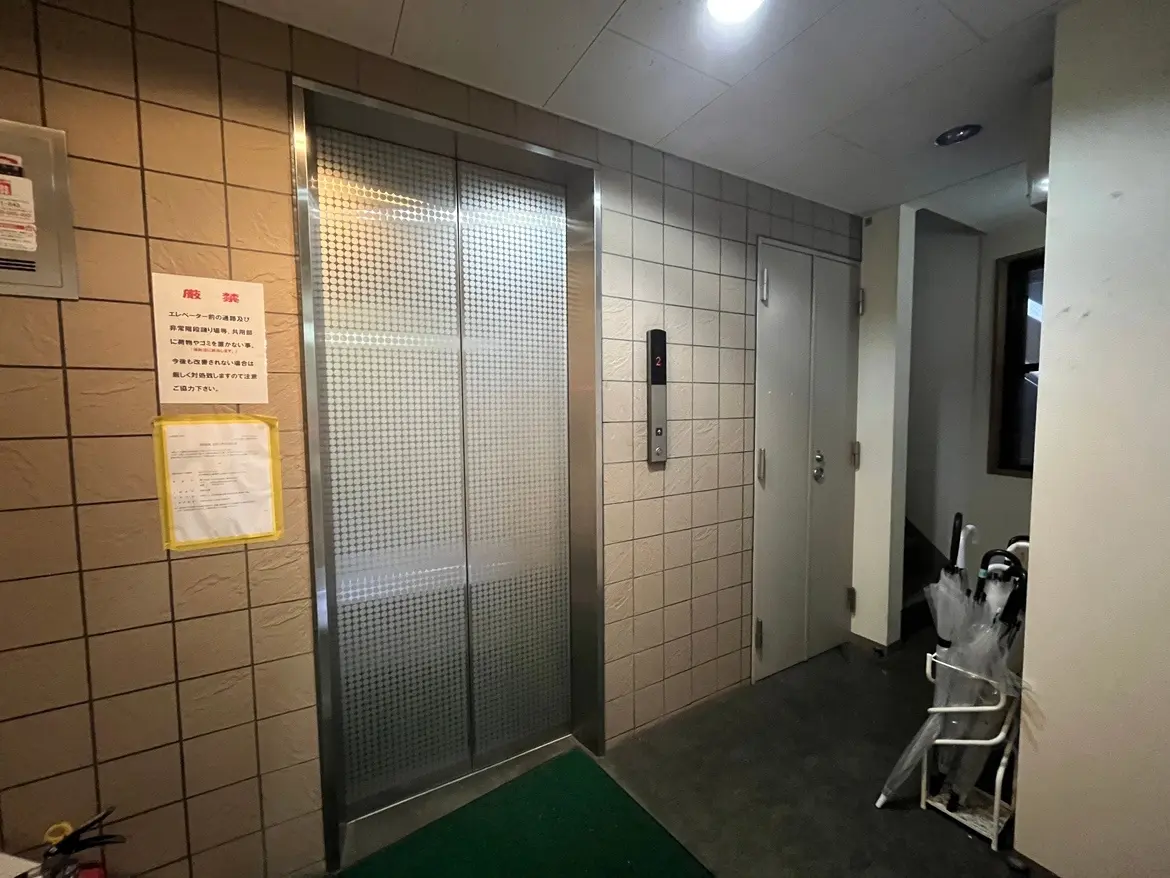 - 建物のエントランス付近に設置された昇降用エレベーターと周囲の様子、注意書きと傘立てがある内部風景