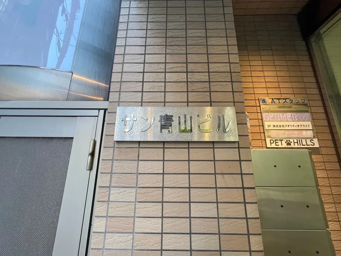 - サン青山ビルの入口、スタイリッシュな看板とタイル張りの壁、近隣の店舗情報が記載されたサインボード