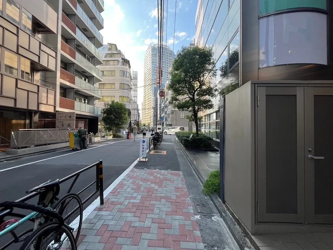 - 近代的なビルが立ち並ぶ街並み、舗装された歩道と自転車が置かれたスペース、青空が広がる中の静かな通りの風景