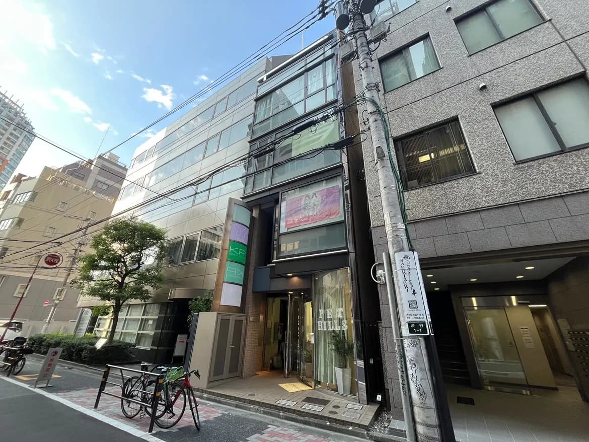 - 都会的なデザインの商業ビル、ガラス張りの外観とアートのサイン、周囲には自転車スタンドと街路樹がある風景