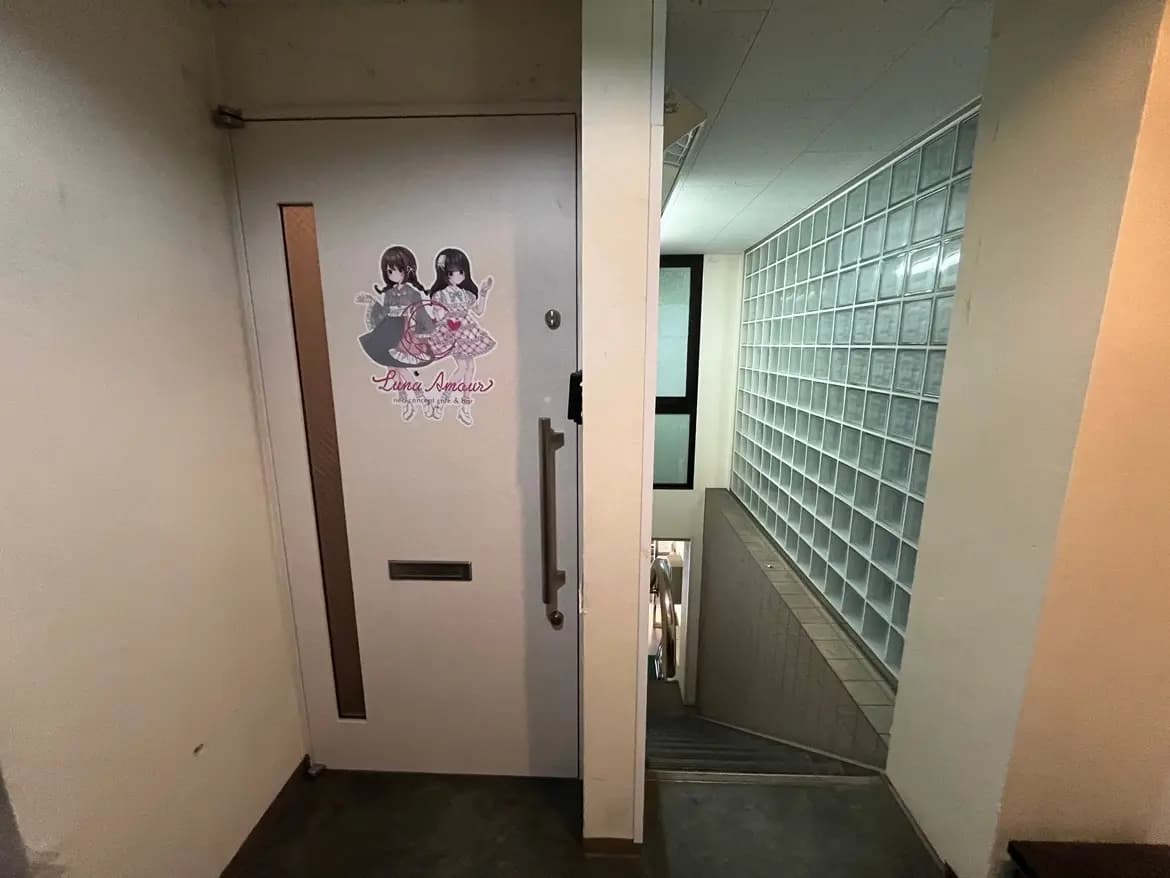 - キャラクターが描かれた白いドアとガラスブロックの壁を背景にした階段の入口、右側に進むと明るい手すりのある階段が見えるインテリア