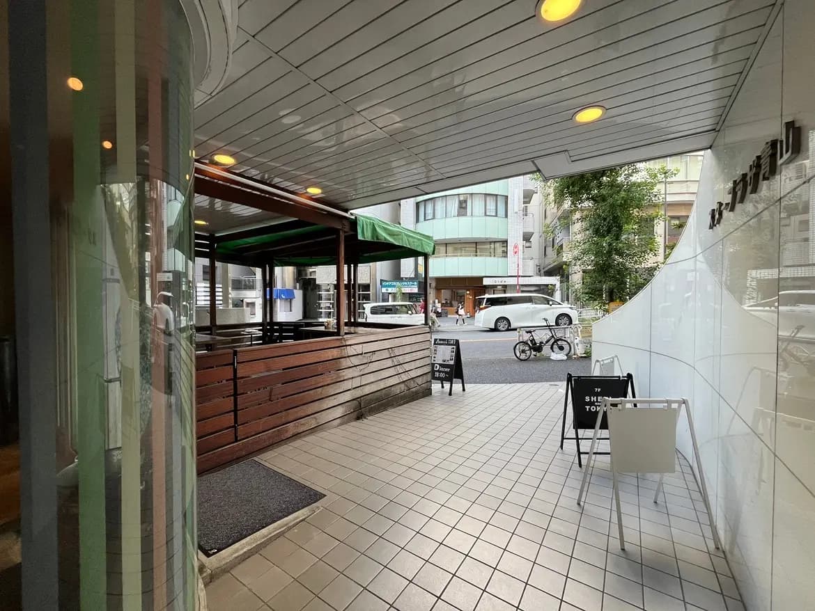 - 繁華街にある飲食店のエントランス、木のブロックで囲まれたテラス席と白い看板が並ぶ歩道