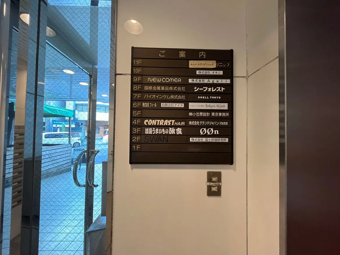 - ビル内のフロア案内板、各階の店舗情報が表示されている明るいエントランスの風景