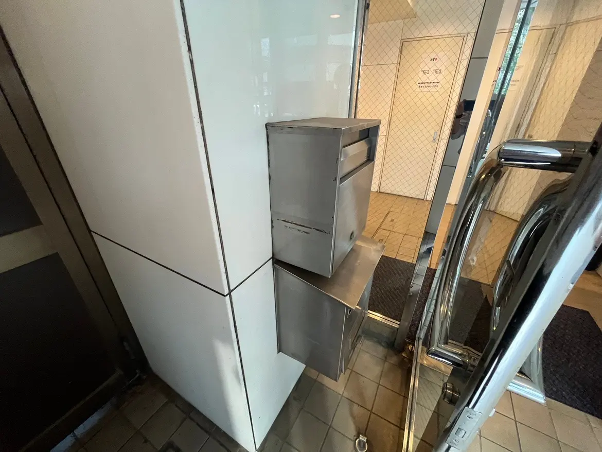 ビルの入り口に設置された金属製の郵便受け、白い壁に取り付けられたシンプルなデザイン。