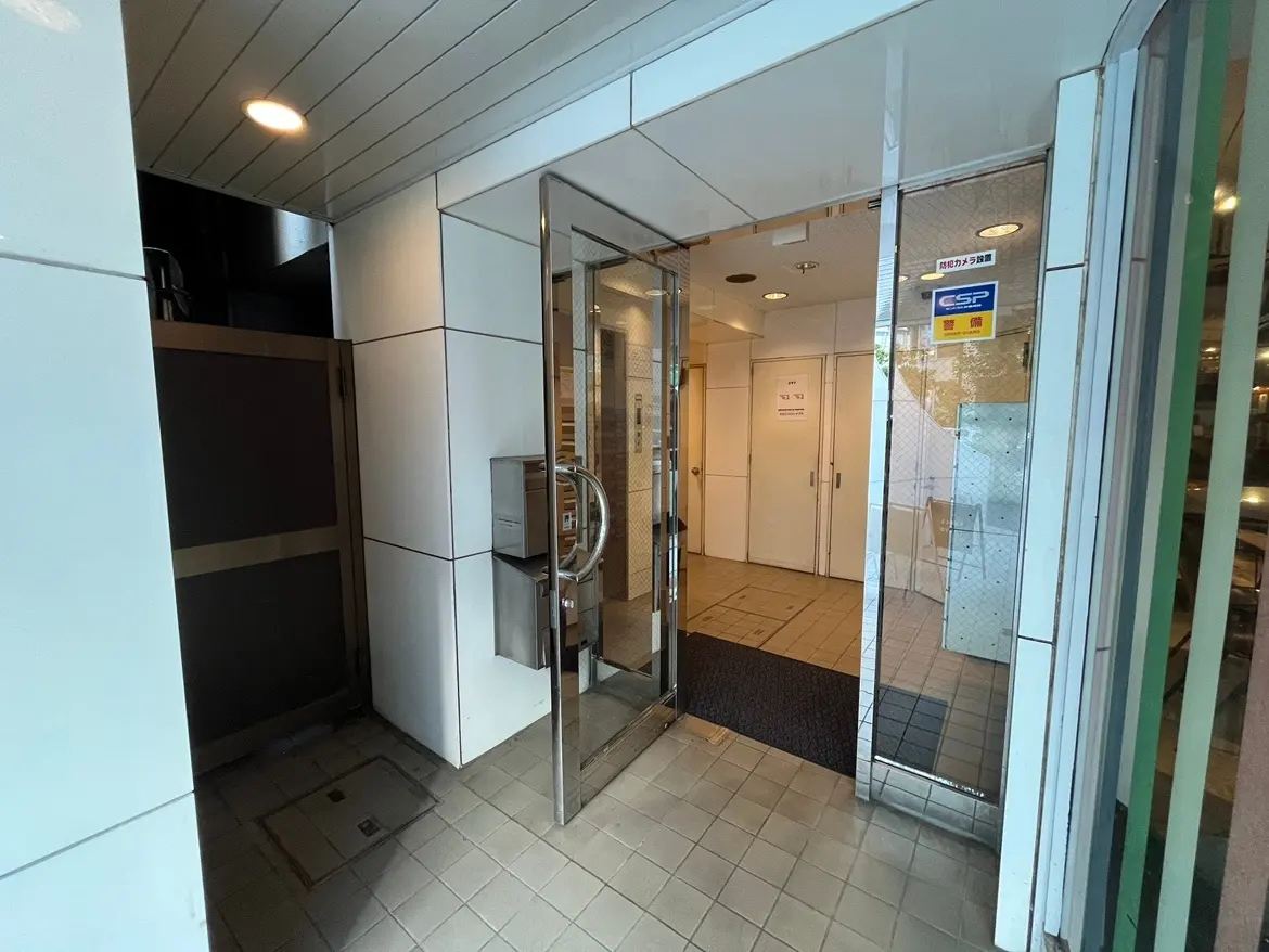 - 現代的なビルのエントランス、ガラスドアとシンプルなタイルフロア、閉じられたドアと郵便受けのある風景