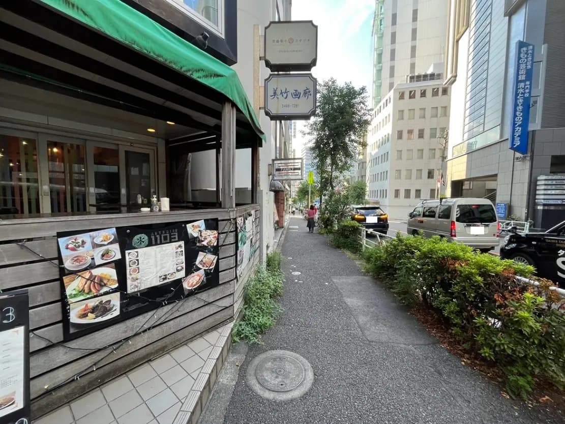 - 東京のビジネス街に位置する和食レストランの外観、メニューが掲示された木製のフェンスと周囲の街並みが見えるシーン