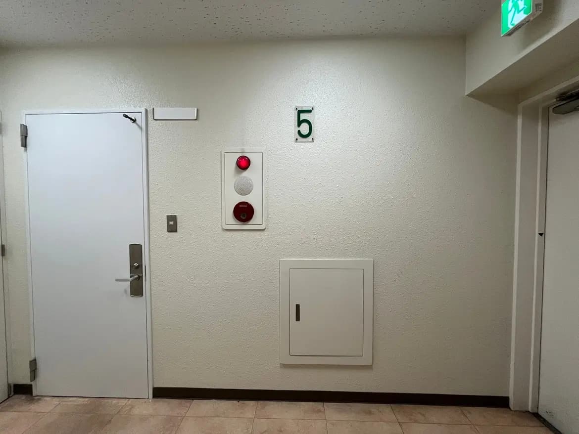 - 白い壁に緑色の数字「5」が表示された廊下、火災警報器とドア、収納スペースがあるシンプルなエントリーウェイ