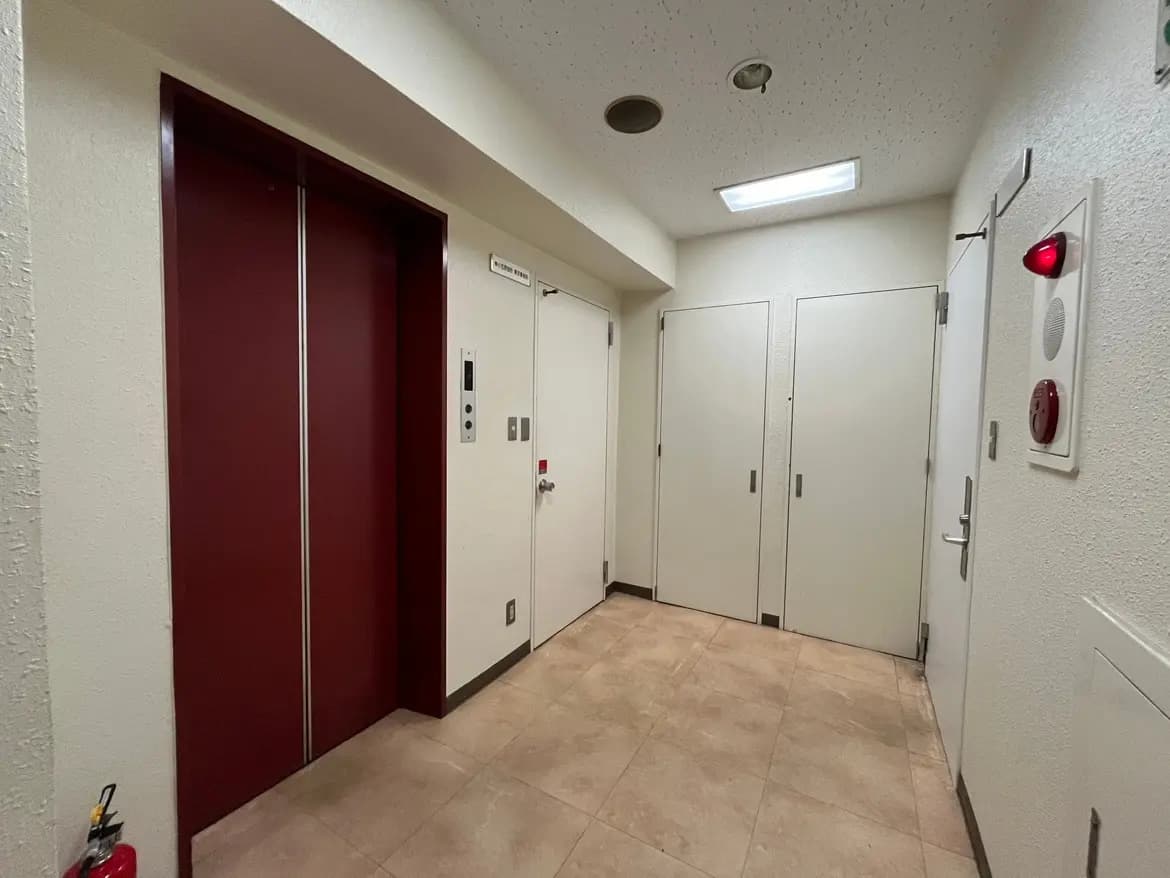 - エレベーターと白い壁がある廊下、床はタイル張りで、異なる種類のドアが並ぶ明るいインテリア