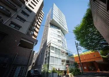 - モダンなデザインの高層ビル、ガラスのファサードと特徴的な形状、周囲の建物と緑豊かな環境の中に立つ様子
