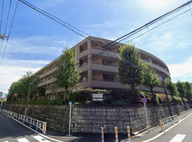 - 自然に囲まれたモダンなアパートメントビルの外観、緑豊かな植栽と青空が広がる風景