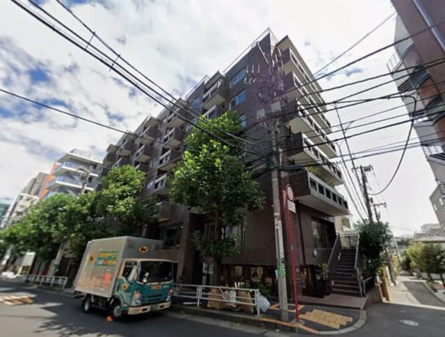 - 都市のアパートメントビル、周辺に緑豊かな木々と交通量のある街並み、配送トラックが近くに停車している風景