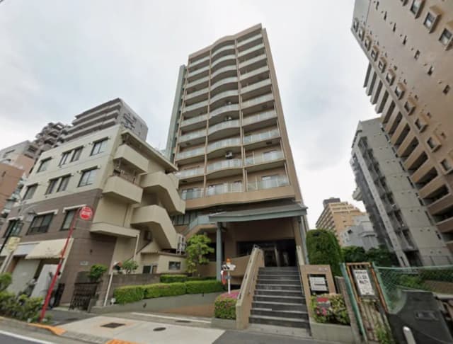 - 都市部に立地する現代的な高層マンション、周囲には他のビルが建ち並び、エントランスには植栽が施された景観