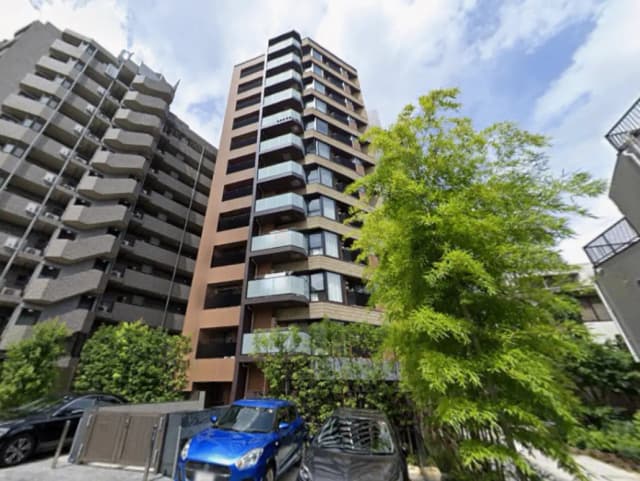 - 近代的なデザインの高層マンション、手前には緑の木々と駐車場に並ぶ車がある風景
